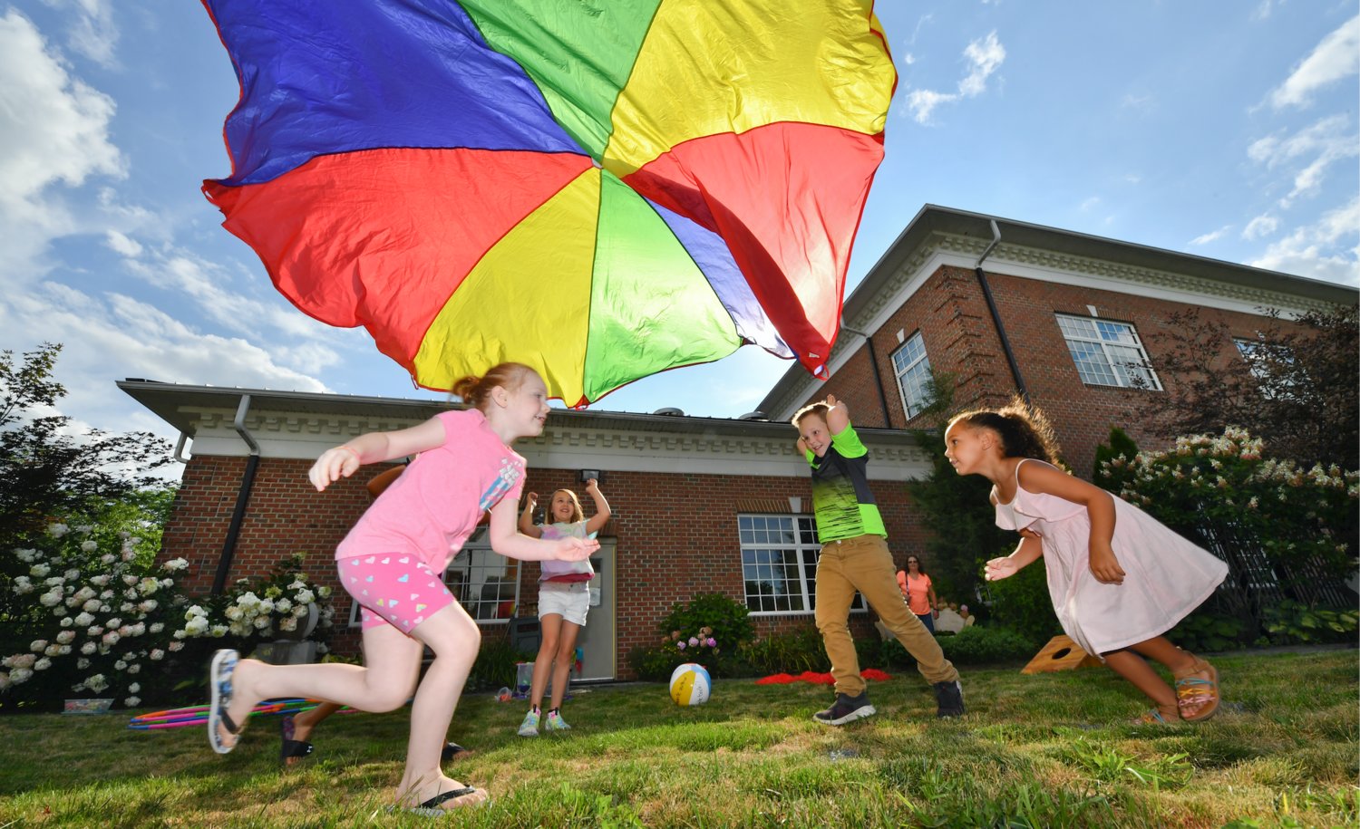 Several kids run under a small parachute after throwing it up in the air while playing a game at the McBride Memorial Library Garden Party at the end of their Summer Reading Party Tuesday, Aug. 3, 2021 in Berwick, PA.